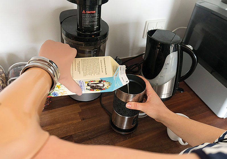 Kvinde med bionisk hånd hælder mælk i en kop - Sahva